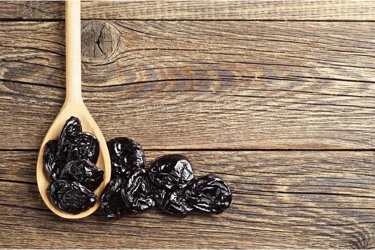 Prunes in a wooden spoon on a wooden table